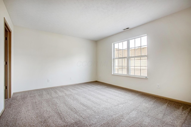 spare room with carpet floors, visible vents, a textured ceiling, and baseboards