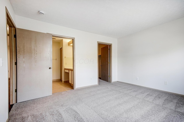 unfurnished bedroom with light carpet, ensuite bath, a walk in closet, and baseboards