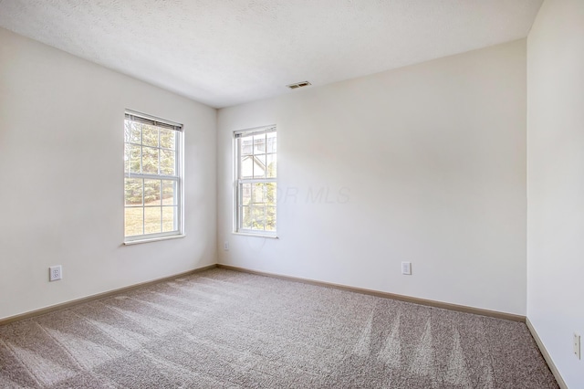 carpeted empty room featuring baseboards, visible vents, and a textured ceiling