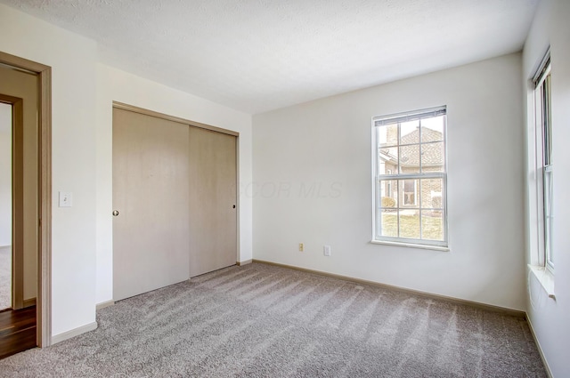 unfurnished bedroom with carpet, a closet, a textured ceiling, and baseboards