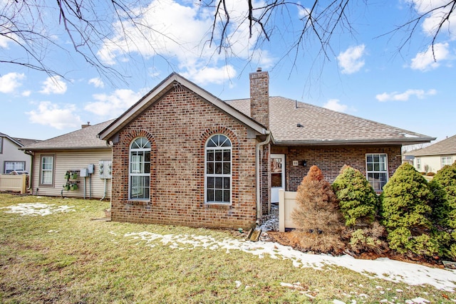 back of property featuring brick siding, a yard, a chimney, and roof with shingles