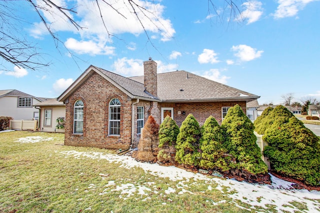 snow covered property with roof with shingles, a chimney, a lawn, and brick siding