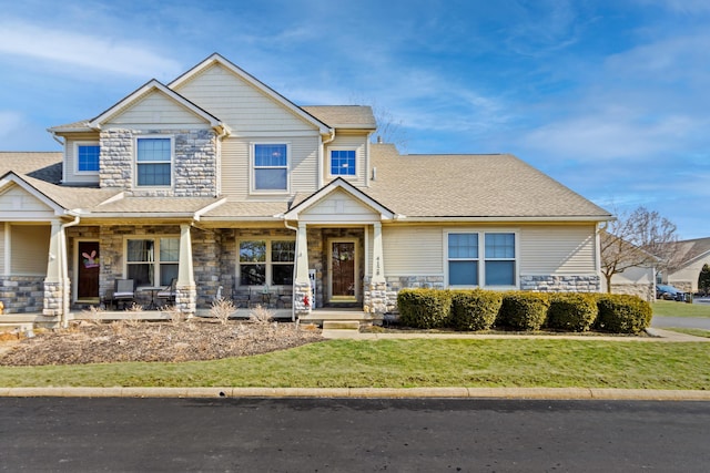 craftsman-style home with stone siding, a porch, a front lawn, and roof with shingles