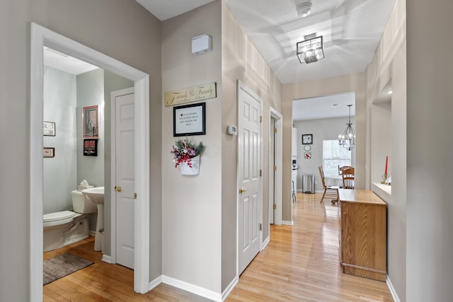 hall featuring light wood-style flooring, baseboards, and a chandelier