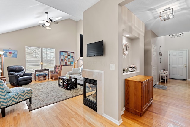 living area with baseboards, a ceiling fan, light wood-style flooring, a fireplace, and high vaulted ceiling