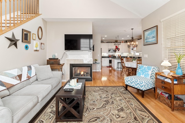 living room featuring a chandelier, lofted ceiling, a warm lit fireplace, and light wood-style floors