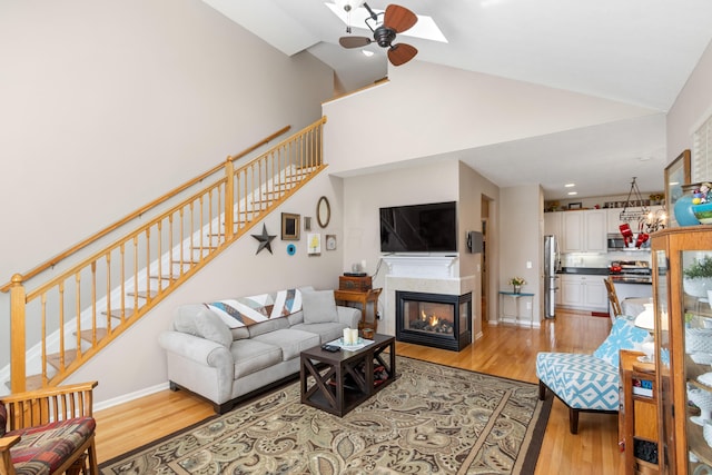 living area featuring stairs, ceiling fan, a multi sided fireplace, and light wood-style floors