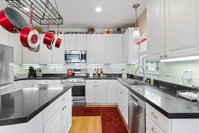 kitchen featuring decorative light fixtures, stainless steel appliances, light wood-style floors, white cabinets, and a sink