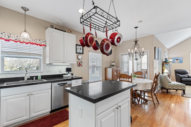 kitchen featuring dark countertops, white cabinets, a kitchen island, a sink, and dishwasher