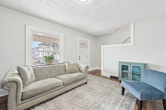 living area featuring a textured ceiling, baseboards, and wood finished floors