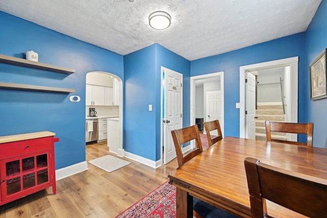 dining area with arched walkways, a textured ceiling, light wood-type flooring, baseboards, and stairs