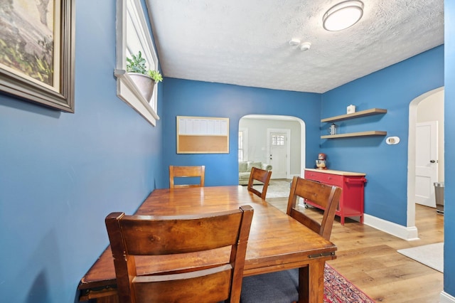 dining room featuring light wood-type flooring, arched walkways, a textured ceiling, and baseboards