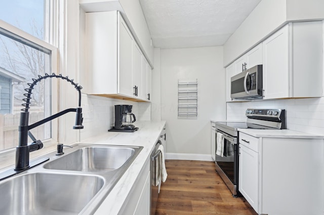 kitchen featuring stainless steel appliances, dark wood-type flooring, white cabinets, a sink, and baseboards