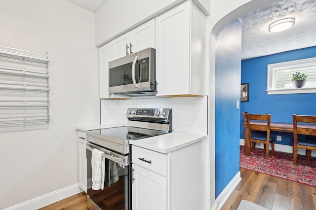 kitchen with appliances with stainless steel finishes, arched walkways, wood finished floors, and tasteful backsplash