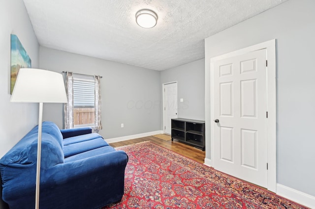 living room featuring a textured ceiling, baseboards, and wood finished floors