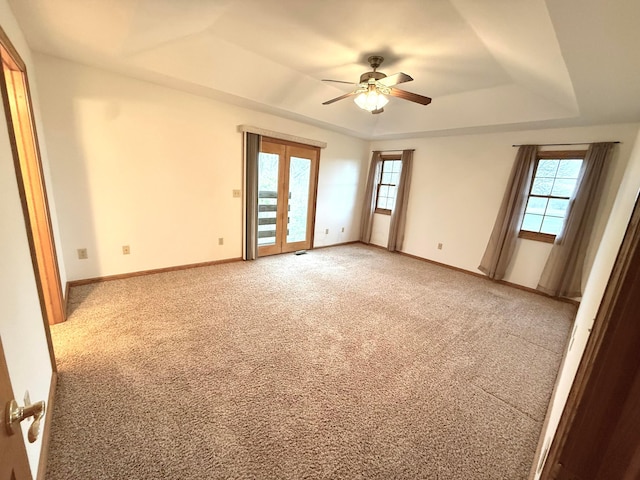 spare room featuring a tray ceiling, light carpet, a healthy amount of sunlight, and ceiling fan