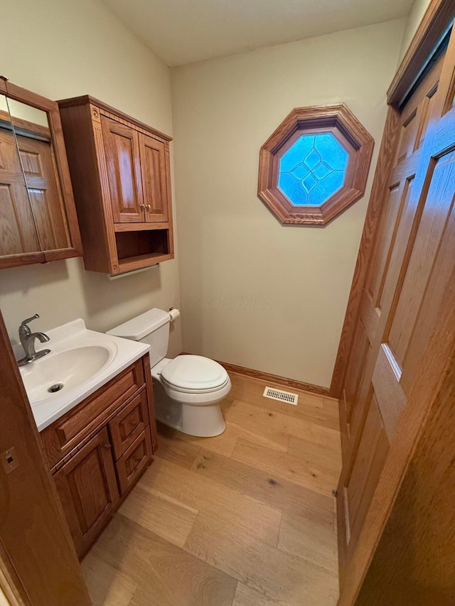 half bath with vanity, wood finished floors, baseboards, visible vents, and toilet