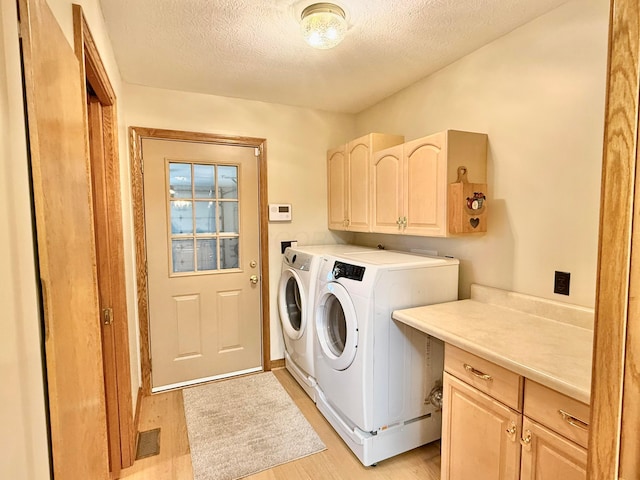 laundry area with visible vents, a textured ceiling, cabinet space, light wood finished floors, and washing machine and clothes dryer