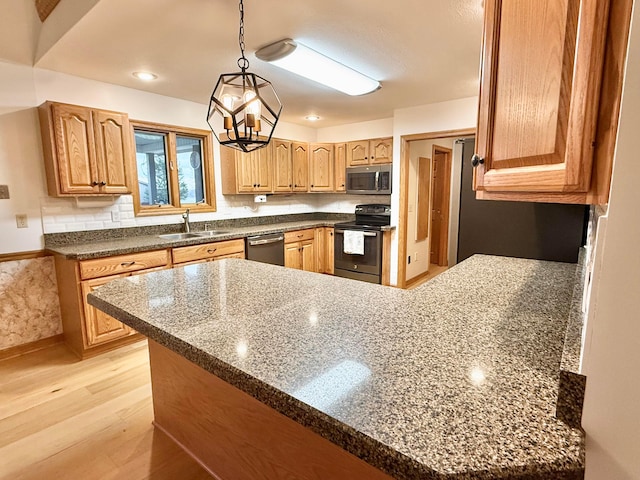 kitchen featuring light wood-style flooring, appliances with stainless steel finishes, a peninsula, an inviting chandelier, and a sink