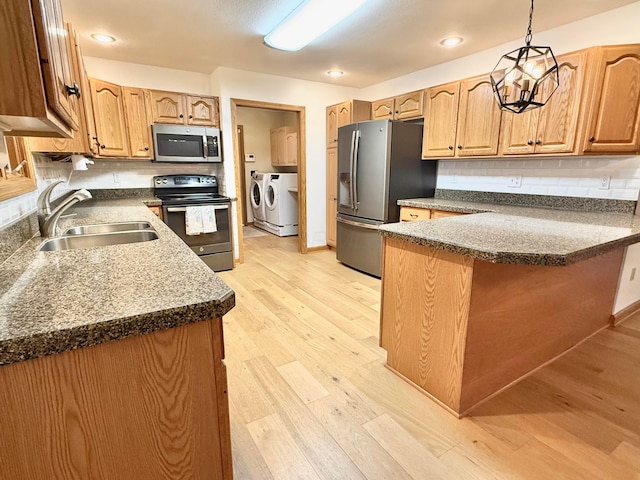 kitchen featuring a peninsula, a sink, stainless steel appliances, washer and dryer, and light wood-type flooring