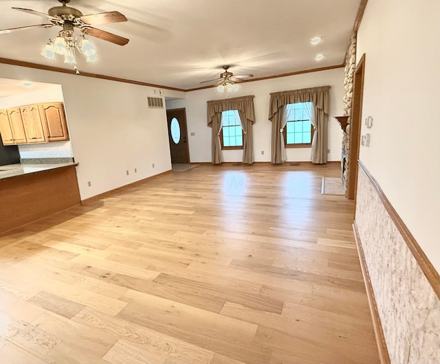 unfurnished living room featuring a ceiling fan, visible vents, baseboards, light wood-style flooring, and crown molding
