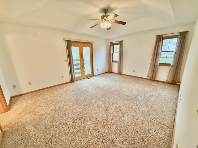 unfurnished room featuring light carpet, a healthy amount of sunlight, a raised ceiling, and a ceiling fan