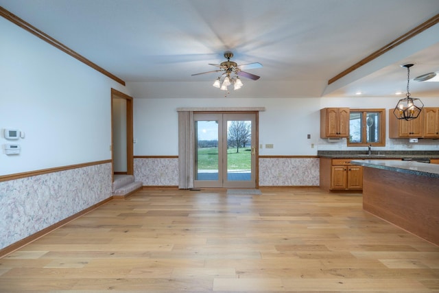 kitchen with a wainscoted wall, light wood-style flooring, wallpapered walls, ceiling fan, and hanging light fixtures