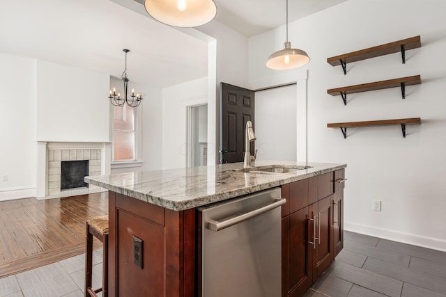 kitchen featuring a center island with sink, dishwasher, a fireplace with flush hearth, wood tiled floor, and a sink