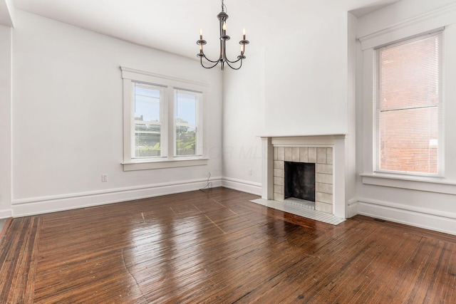 unfurnished living room featuring baseboards, dark wood-style flooring, a tiled fireplace, and an inviting chandelier