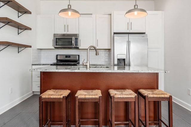 kitchen with a sink, white cabinets, appliances with stainless steel finishes, light stone countertops, and tasteful backsplash