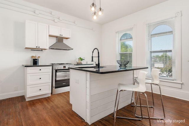 kitchen with dark countertops, wall chimney exhaust hood, a breakfast bar, and gas stove