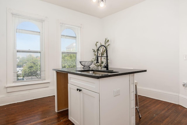 kitchen with a sink, white cabinetry, dark countertops, a kitchen bar, and a center island with sink