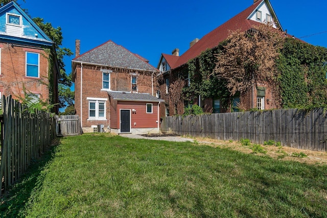 rear view of property featuring a fenced backyard, an outbuilding, cooling unit, a yard, and brick siding