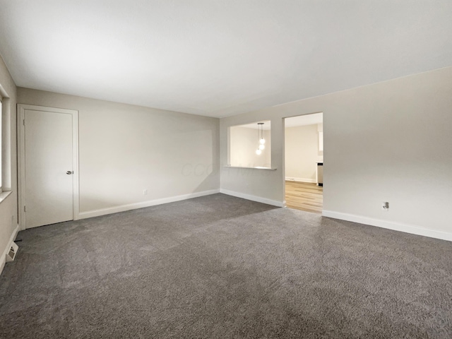 empty room featuring visible vents, dark carpet, and baseboards