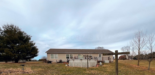 rear view of house with an outdoor pool, a deck, and a lawn