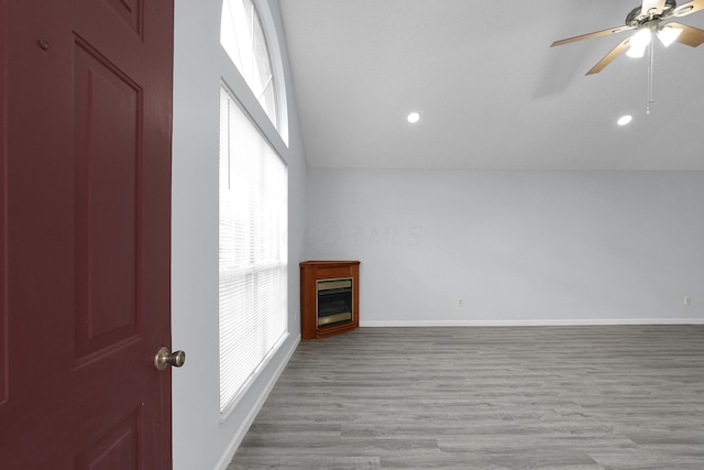 unfurnished living room with a ceiling fan, baseboards, vaulted ceiling, light wood-style floors, and a glass covered fireplace