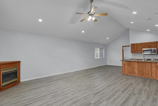 unfurnished living room featuring light wood finished floors, a glass covered fireplace, ceiling fan, high vaulted ceiling, and baseboards