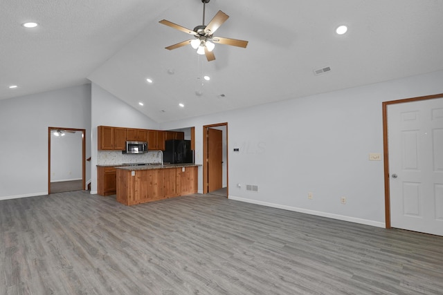 kitchen featuring brown cabinets, stainless steel microwave, light wood-style flooring, freestanding refrigerator, and open floor plan