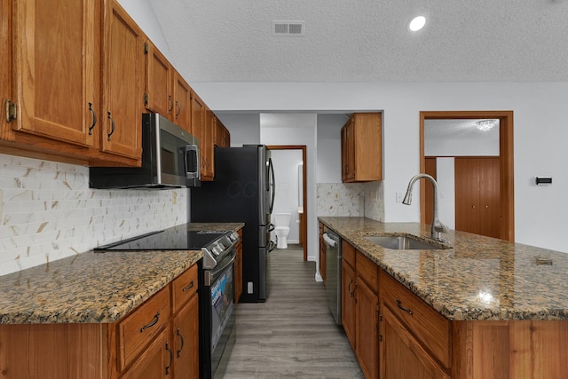 kitchen featuring appliances with stainless steel finishes, brown cabinetry, a sink, and visible vents