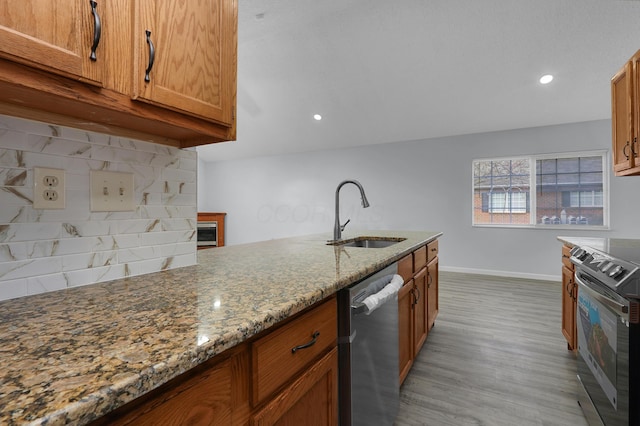 kitchen with brown cabinetry, a sink, light stone countertops, stainless steel appliances, and backsplash