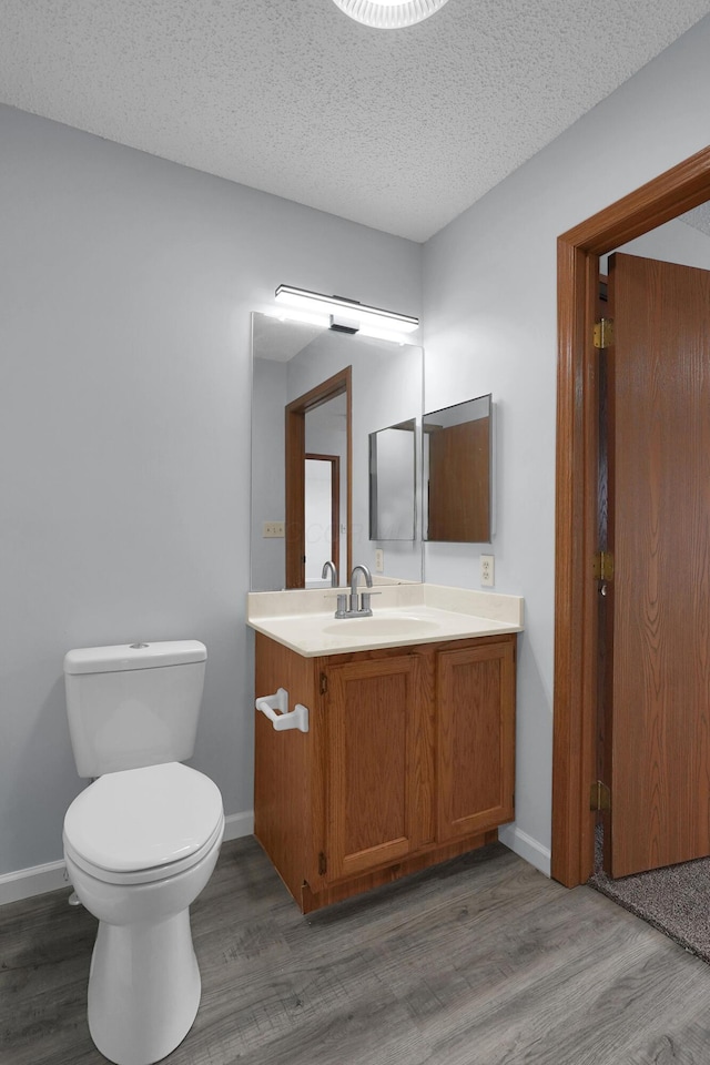 half bathroom featuring a textured ceiling, toilet, wood finished floors, vanity, and baseboards