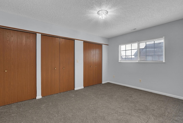 unfurnished bedroom with dark carpet, a textured ceiling, baseboards, and two closets