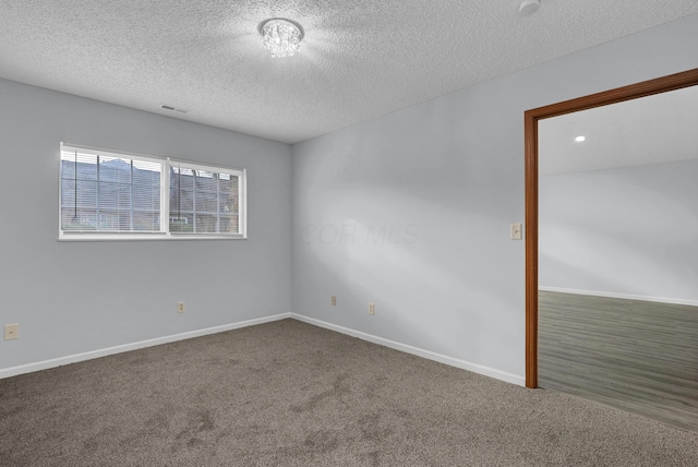 spare room with a textured ceiling, dark colored carpet, visible vents, and baseboards