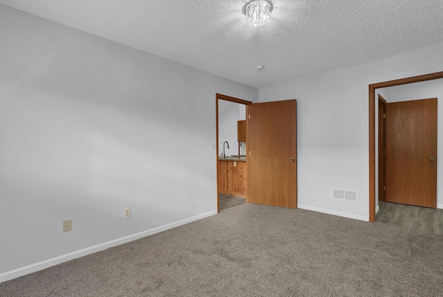 unfurnished bedroom featuring a textured ceiling, a sink, visible vents, baseboards, and carpet