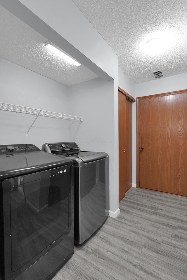 laundry room with a textured ceiling, laundry area, light wood-style floors, baseboards, and washer and dryer