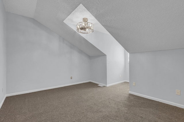 bonus room with baseboards, vaulted ceiling, dark colored carpet, a textured ceiling, and a notable chandelier