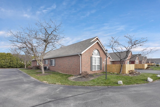 view of home's exterior with a yard, roof with shingles, fence, and brick siding