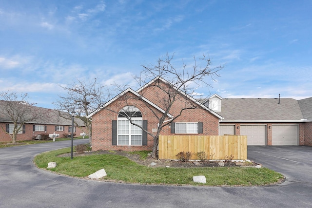 view of front of property featuring an attached garage, brick siding, fence, driveway, and roof with shingles