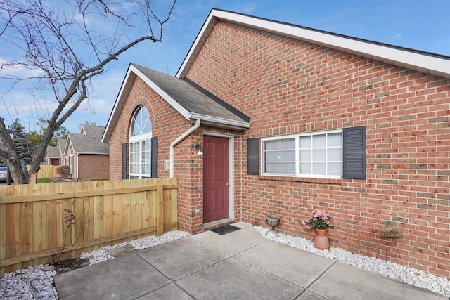 view of front facade featuring brick siding, a patio area, fence, and a shingled roof