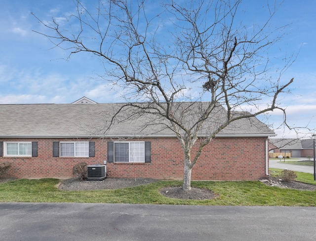 view of side of property with a shingled roof, a lawn, central AC, and brick siding